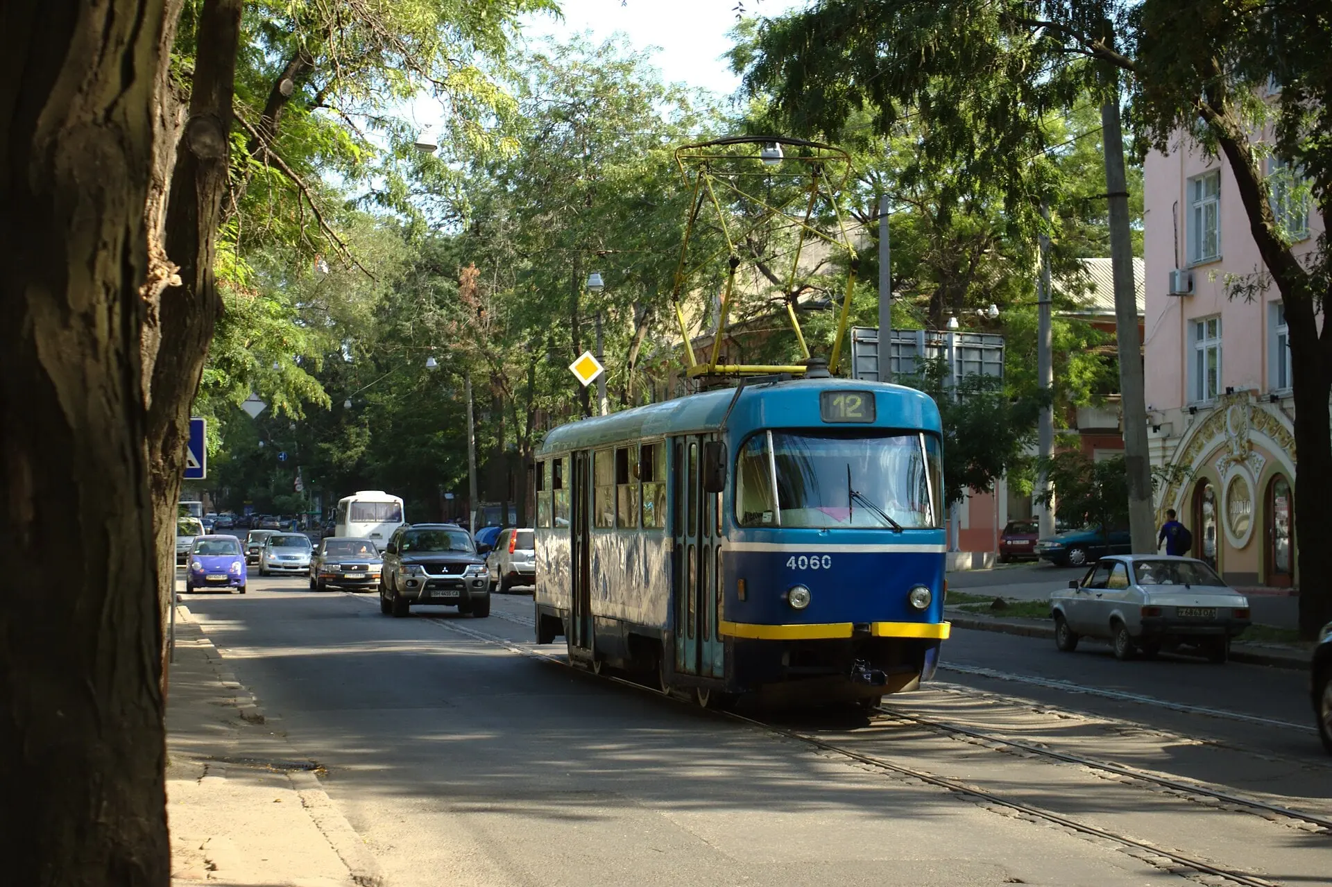 Синій одеський трамвай на вулиці під деревами